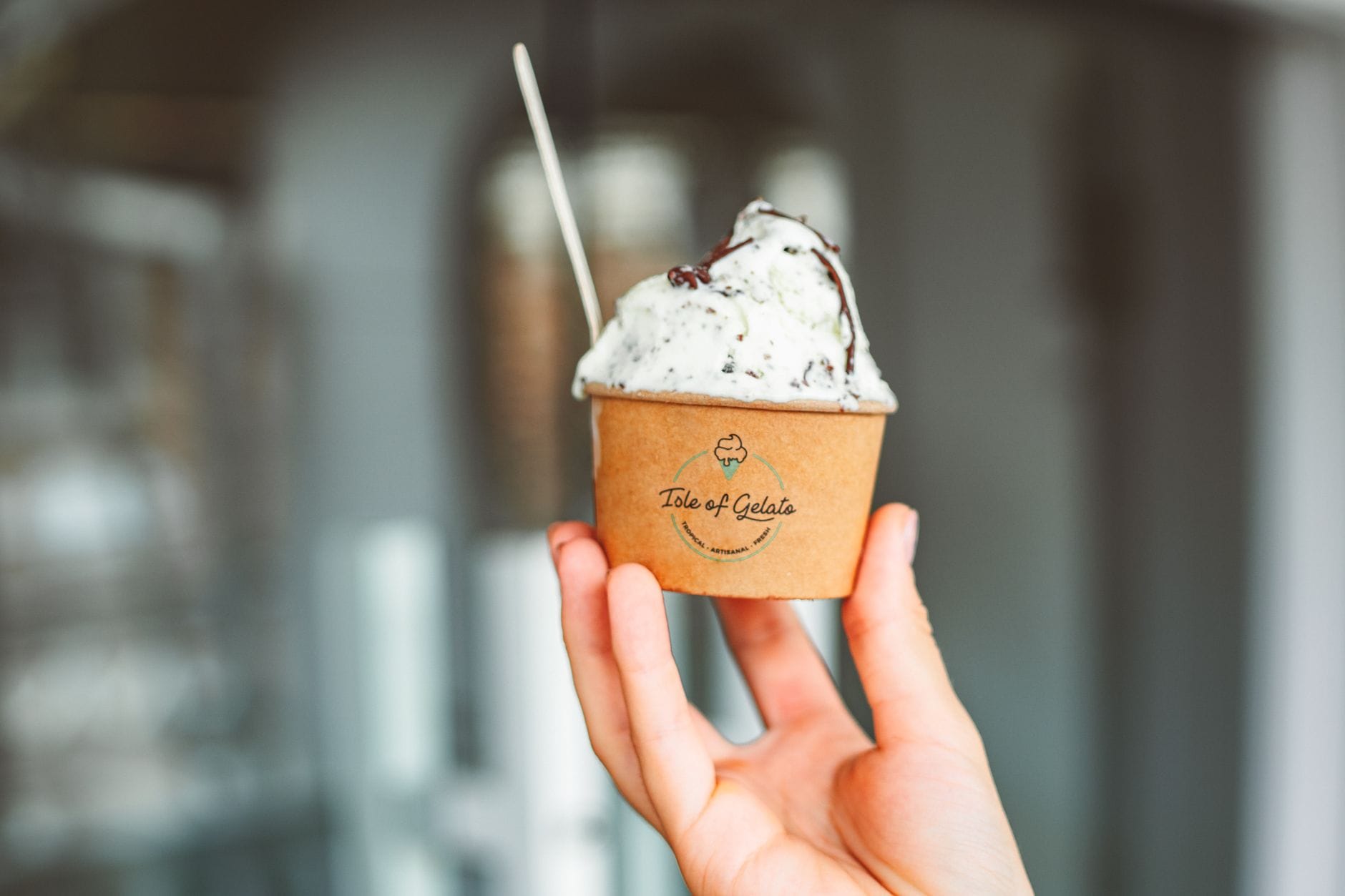 Dłoń trzyma kubek kremowego gelato z łyżeczką w tle miasta