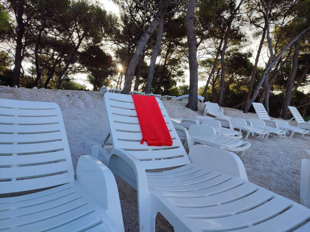 Spokojna plaża w Chorwacji z leżakami i czerwonym ręcznikiem